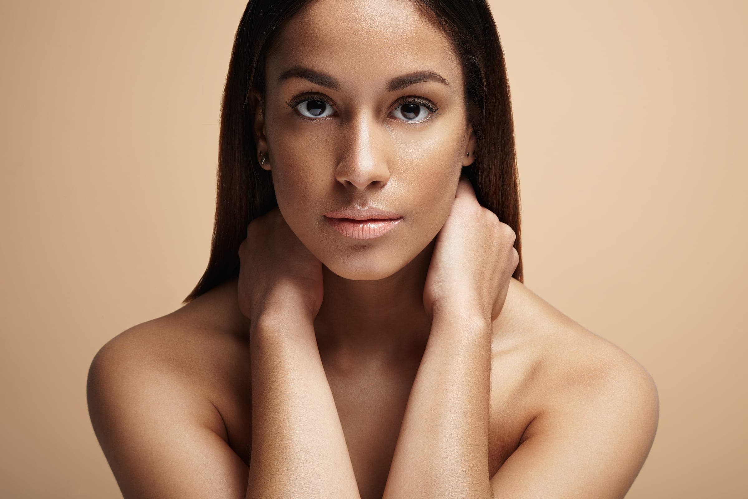 Woman with natural, glowing skin against a warm beige backdrop